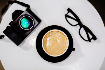 Top view of camera,  coffee and glasses on  on white round table.