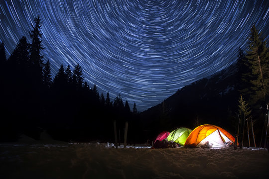 Night camp with illuminated tents in the mountain landscape with star trails in the sky