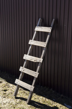 Uneven Home Made Wooden Ladder With Visible Nail Heads Standing At Corrugated Iron Wall