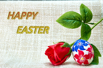 A rose flower near an easter egg hand-painted on a beautiful tablecloth