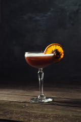 Hot mulled wine with foam with a slice of orange on a wooden table over dark background