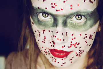 Mujer joven con un maquillaje de carnaval lleno de purpurina con forma de estrellas rojas 