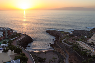 Sunset of the seascape. La Gomera island is on horizon. Coast of Playa Paraiso village with ocean waves breaking cliffs. Tenerife, Canary islands. Spain