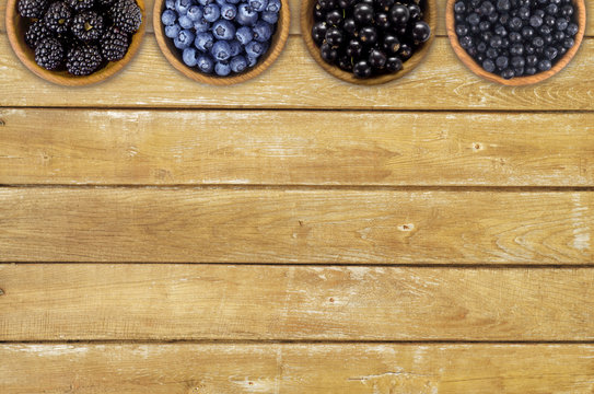 Black and blue berries. Blackberries, blueberries, currants and blueberries in a wooden bowls. Berries at border of image with copy space for text. Top view.