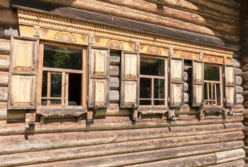 Traditional rural Russian ancient architecture. Windows of old log house with carved wooden trim