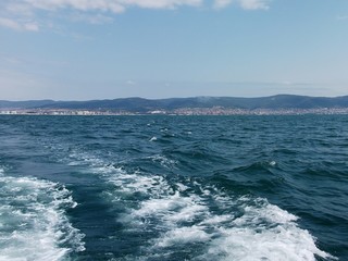 Black sea surface summer wave background. View from yacht. Exotic seascape with clouds and town on horizon. Sea nature tranquility (Bulgaria, Sunny Beach)