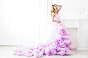 Dreamy woman portrait in a long pale purple ruffled gown in a white room. Elegant femininity