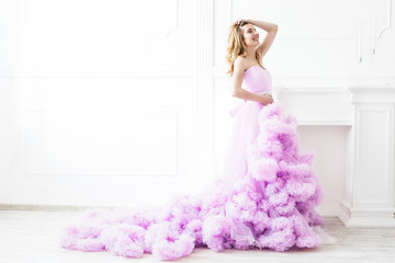 Dreamy woman portrait in a long pale purple ruffled gown in a white room. Elegant femininity