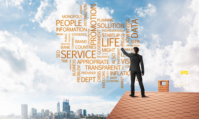 Young businessman standing on house roof and writing leadership skill concept. Mixed media