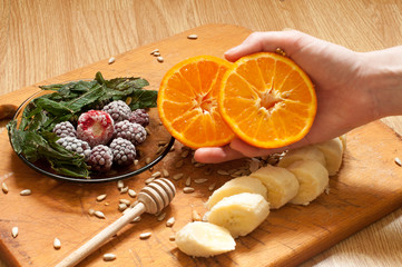 cooking, banana,hand holding orange,frozen strawberries blackberries and seeds vivid smoothie ingredients and blender, juicer, tulips on the background