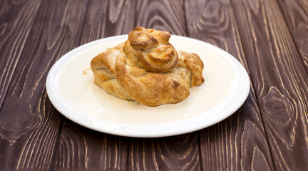 Piece of puff cake with meat on a white plate. Wooden background