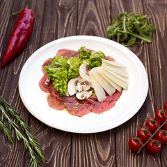 Beef carpaccio salad in white plate on wooden background.