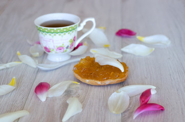 Fototapeta na wymiar Bread with homemade jam on wooden background. Cup of tea and flower petals. Selective focus.