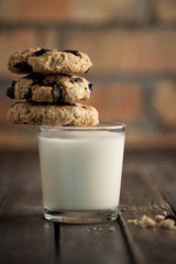 A glass of milk and cookies with raisins. A wooden table and a brick wall on a background. Selective 
focus.
