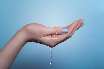 A picture of a woman's hand on which water flows, on a blue background.