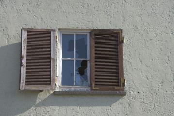 Altbaufassade mit einem kaputten Fenster und großer verputzter Wandfläche