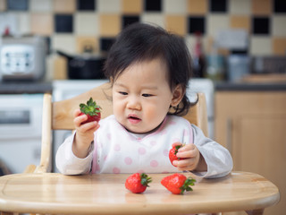 Asian baby girl eating  strawberry at home kitchen