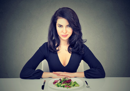 Attractive young woman sitting at table ready to eat green salad