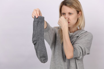Female gesture smells bad. Woman holding a dirty sock out of washing basket with a disgusted look...