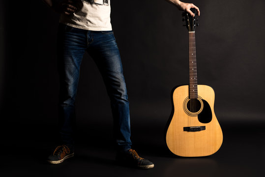Guitarist holding his left hand with an acoustic guitar on a black isolated background