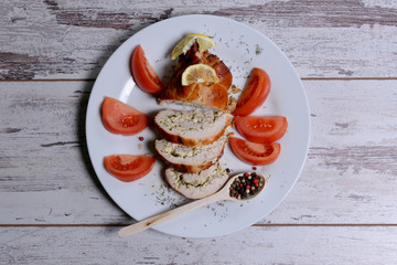 Baked chicken rolls with tomato and lemon and spices on white plate on a white wooden table