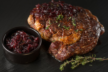 Pork steak on black stone plate. Black table background with copy text area for menu design. Horizontal top view.