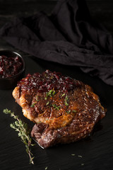 Beef steak and sauce with onion and herbs on black stone plate. Black table background with copy text area for menu design. vertical top view.