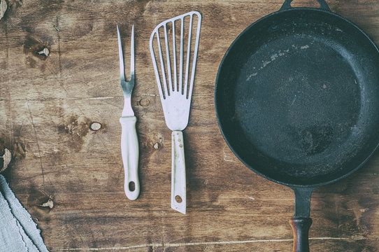 Empty black cast-iron frying pan with vintage kitchen items on a brown table