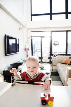 8 month old baby boy smiling and playing with toy at adult table in penthouse