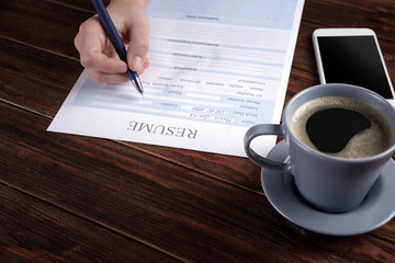 Woman filling resume form on wooden table, closeup