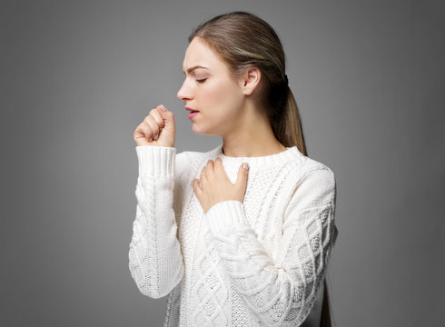 Young woman coughing on gray background