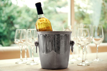 Wine bottle in bucket with ice and glasses on table