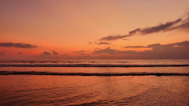 Slow motion of sea waves roll on coast of Bali island at orange sunset time
