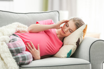 Pregnant woman suffering from headaches while lying on sofa at home