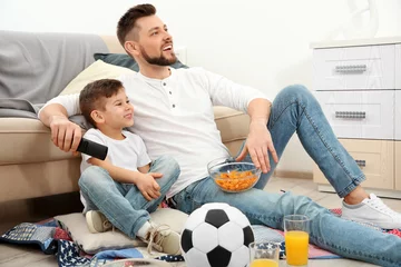 Fotobehang Father and son watching football on TV at home © Africa Studio