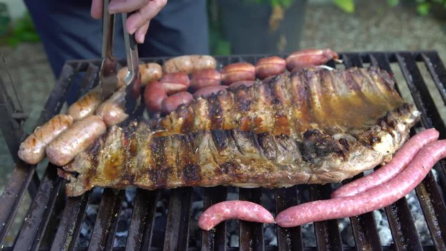 4K Cooking barbecue with delicious sauce on grilled meat. Unhealthy fatty BBQ of Ribs Pork and Sausages, spanish chorizo, Chistorra, Morcilla, Blood sausage being fried on a charcoal grill -Dan
