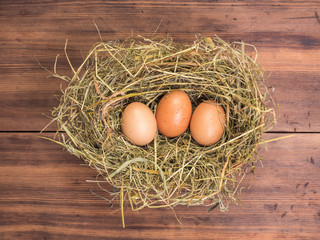 Brown eggs in hay nest. Rural eco background with brown chicken eggs and straw on the background of old wooden planks. Top view. Creative background for Easter cards, restaurant menu or design