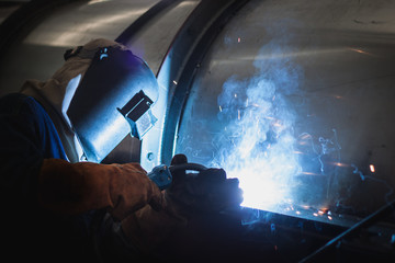 Welder working at welding metal with protective mask and sparks.