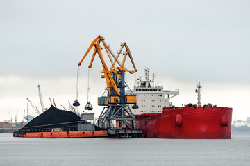 Large red cargo ship loading with a coal in the port