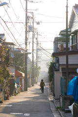 A woman walks along a narrow neighborhood street in Japan.