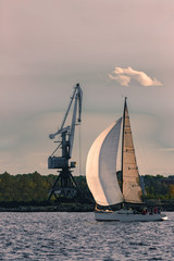 Sailboat moving past the cargo crane in evening, Latvia