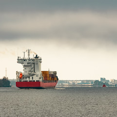 Naklejka premium Red cargo container ship entering the port of Riga in cloudy day