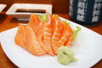 Closeup of fresh salmon sashimi slices on a white plate with sauce and wasabi, Japanese food style