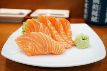 Closeup of fresh salmon sashimi slices on a white plate with sauce and wasabi, Japanese food style