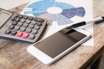 Data analyzing with calculator mobile phone and pen on wooden table background