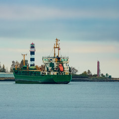 Naklejka premium Green cargo ship moving to the port in cloudy day