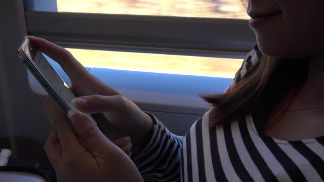 4K Asian Woman Traveling on train. Is a good time to get some work done on phone device, using smartphone for cheks e-mail and writting text, as she waits. Surfing internet, checks social network-Dan