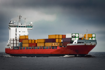 Red cargo container ship sailing from Baltic sea in cloudy day