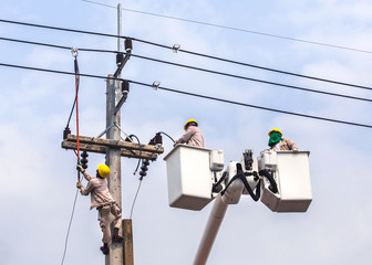                   Electricians repairing wire of the power line with bucket hydraulic lifting platform on blue sky background
