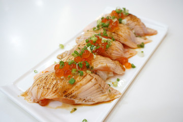 Closeup of salmon sushi on a white plate with salmon roe and chopped spring onion, Aburi style refers to nigiri sushi, the fish is partially grilled topside and partially raw - Japanese food style.